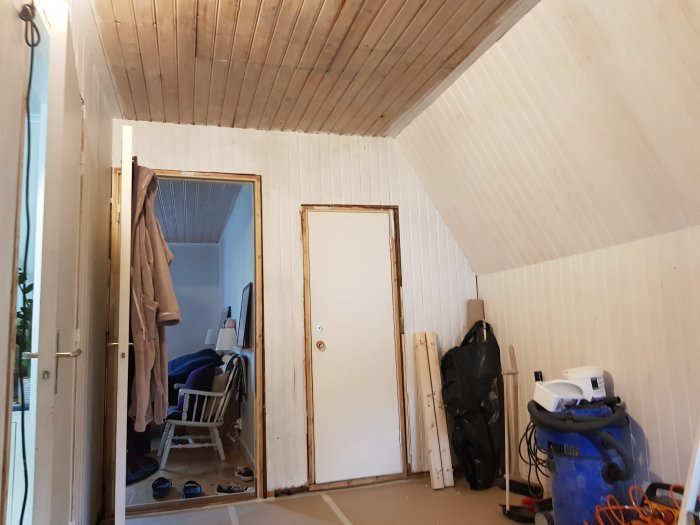 Ett trapphus under renovering med grundmålat träpanel och ommålade väggar, verktyg syns i förgrunden.