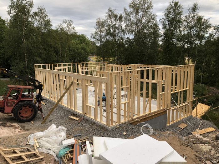 Träregelverk för ytterväggar på ett entréplan står uppe på en byggplats med byggmaterial runtomkring.