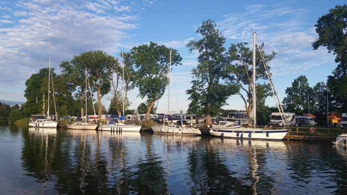 Segelbåtar förtöjda vid en brygga på Wassbacken längs Göta Kanal omgiven av grönska under sommaren.