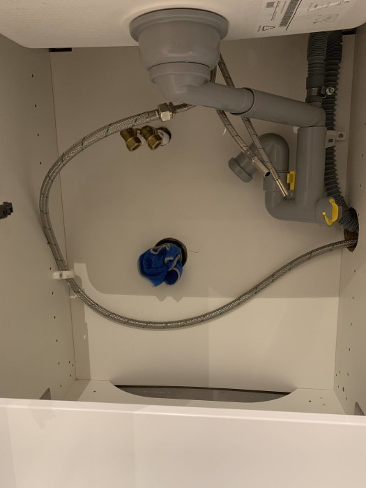 Underskåp med tillfälligt pluggade pex-rör och diskbänksavlopp i väntan på installation av blandare.