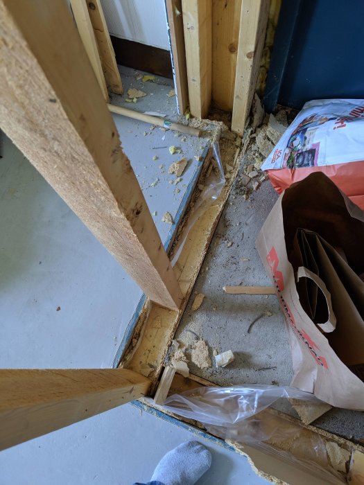 Bild på ett hörn av ett garage med träreglar, isoleringsmaterial, betongplatta och byggavfall.