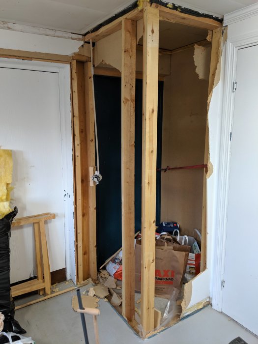 Rumsavdelning med träreglar och osammanhängande gipsväggar inuti ett garage, med synliga skadade områden och renoveringsmaterial.
