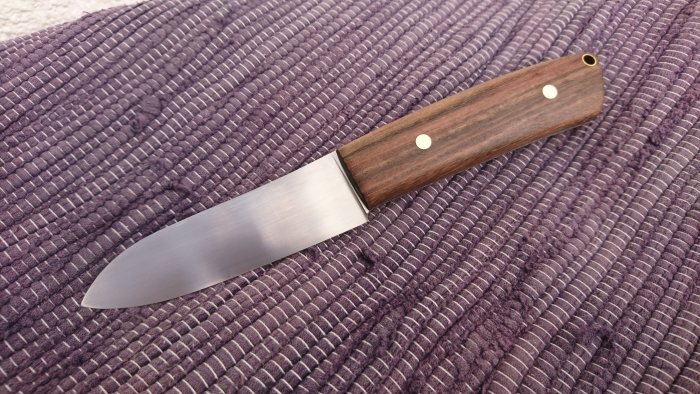 Handgjord kniv med trähandtag och silverfärgat blad på lila textilunderlag.