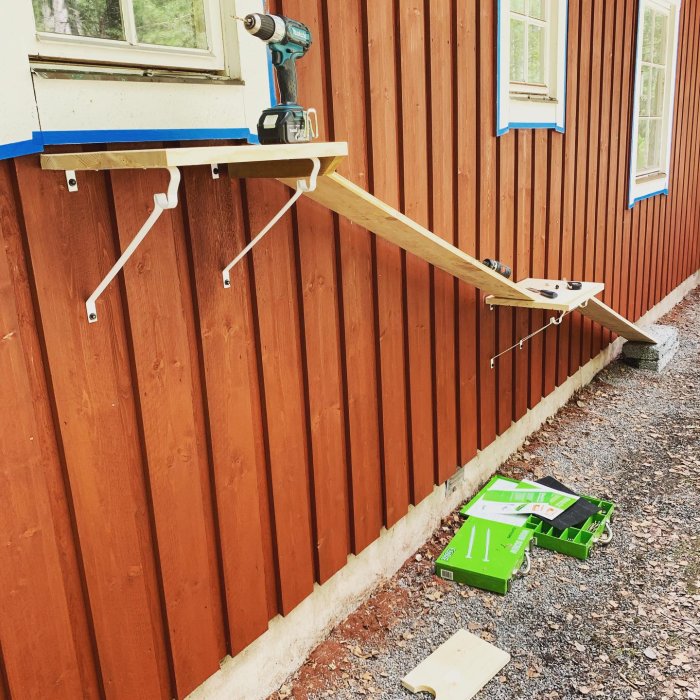 Hembyggd träkattramp monterad på en rödfärgad husvägg med verktyg och material synliga.