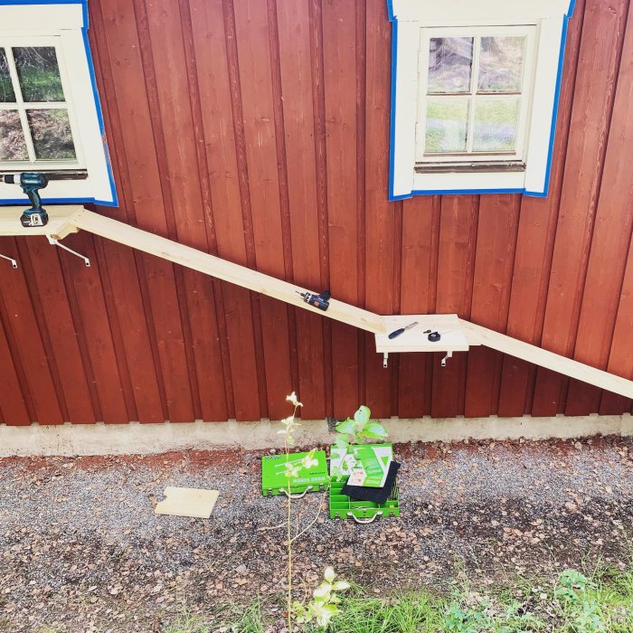 En hemmagjord trärampe som leder upp till ett fönster på ett rödmålat trähus, omgiven av verktyg.