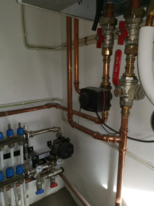 Installation av vattenburen golvvärme med synliga kopparledningar och fördelare i en källare.