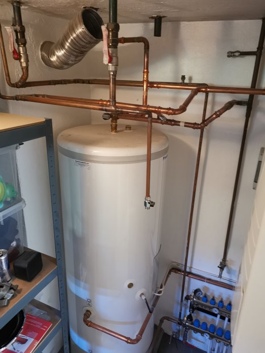 Installationsvy av vattenburen golvvärme och kopparmässiga rörledningar i ett uppvärmningssystem nära en varmvattenberedare.
