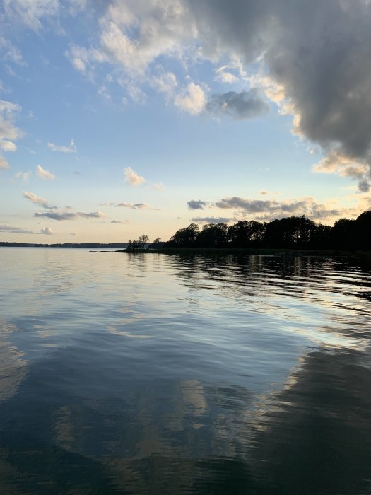 Skymning över en stilla sjö med moln i horisonten som reflekterar omväxlande väder.