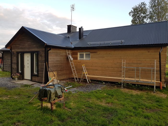 Nypanelad långvägg på husets norrsida med dubbelfönster, stege och renoveringsmaterial i förgrunden.