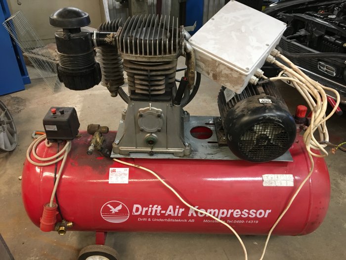 Röd Drift-Air kompressor med motor med YD-start och kopplingsskåp, kablarna och givaren är synliga.