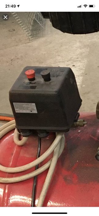 Tryckvakt med svart kontaktstycke och sladd, och mässingsventil, på röd tank.