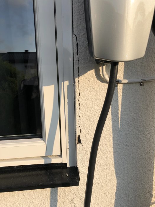 Sprickor i putsad fasad vid ett fönster med synlig skada på betong och puts.