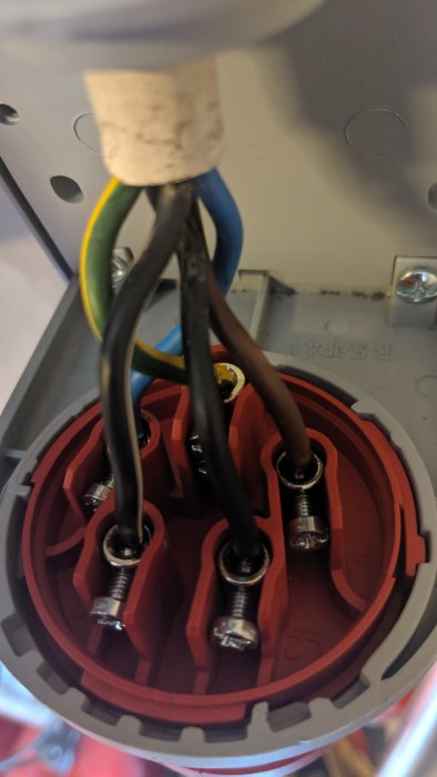 Elkontakt med anslutna kablar i färgerna gul/grön, blå och svart, monterade i en väggkontakt.