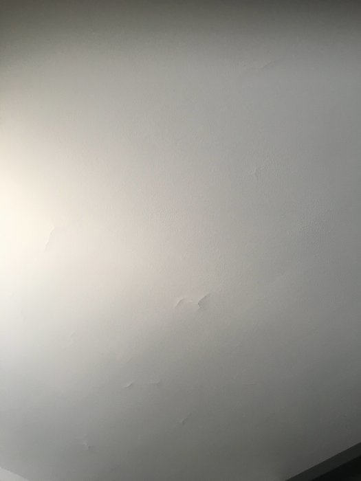 Sprickor i ett vitmålat innertak, med flagnande färg och synliga förändringar i strukturen.