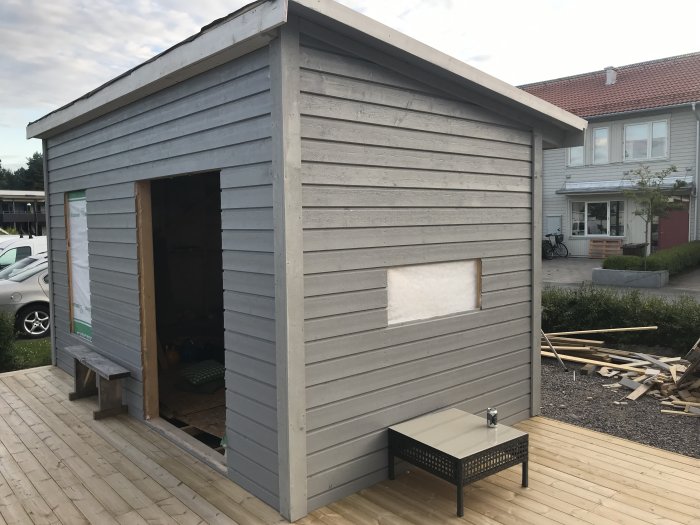 Nybyggt grått träskjul med pågående arbete, utan dörr och fönster, på en altan.