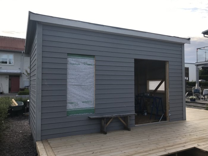 Nybyggt utvändigt trähus i grått före målning med synlig isolering i ett fönsteröppning och tom dörröppning.