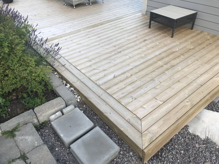 Träaltan med gering på hörnet, intill grönskande växter och en svart uteplatsmöbel.