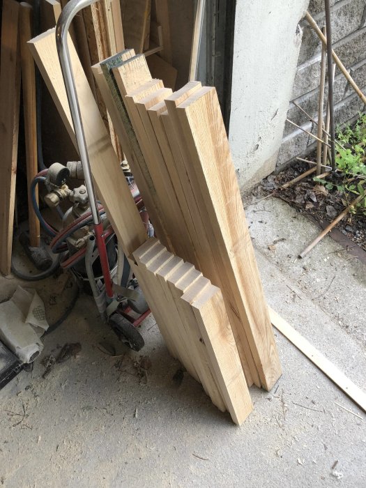 Klyvda träbitar förberedda för limning till skåpluckor, stående mot en vägg i verkstadsmiljö.