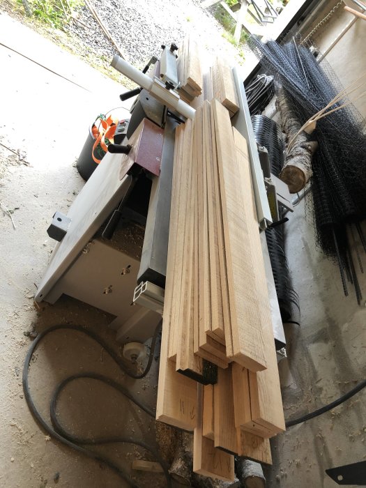 Träbjälkar ordnade i staplar på en arbetsbänk i en verkstad, redo för vidare bearbetning i ett skåpluckeprojekt.