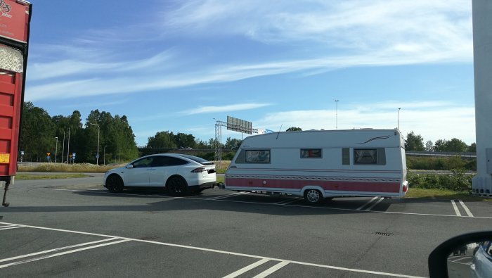 Vit Tesla som drar en husvagn parkerad utanför Biltema under en blå himmel.