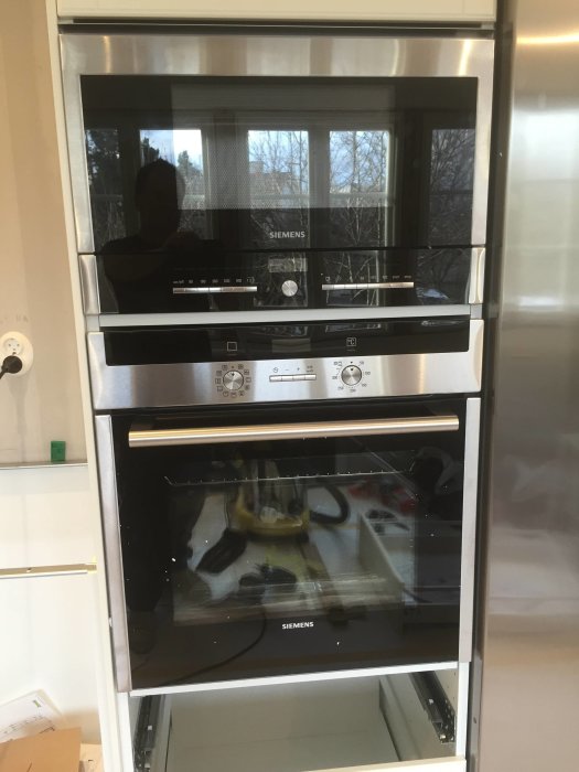 Siemens inbyggda ugn och mikrovågsugn i kök, reflektion och verktyg syns i glaset.