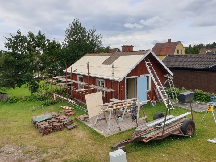 Hus med halvt avtäckt tak, byggställning, gamla pannor staplade på marken och material utspridda.