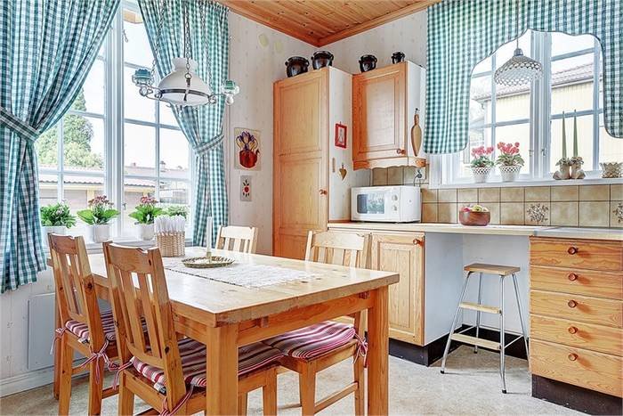 Lantligt kök med träinredning, matbord och stolar, rutiga gardiner och inredningsdetaljer.