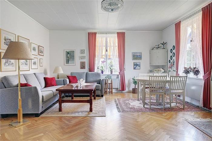 Elegant vardagsrum med soffgrupp, matsalsbord och inredningsdetaljer, parkettgolv och röda gardiner.