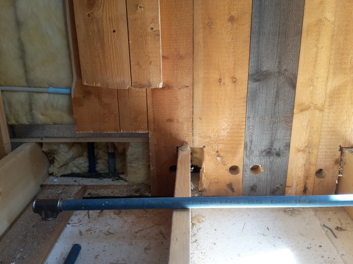 Innertak i utbyggnad med synliga golvbjälkar, rör och isolering, samt borrade hål i bjälkarna.
