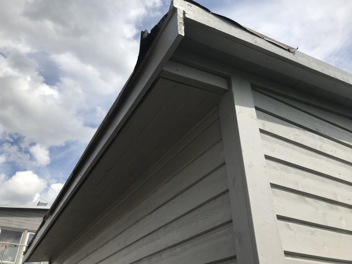 Ny målad träpanel och takutsprång på ett husbygge mot en himmel med moln.