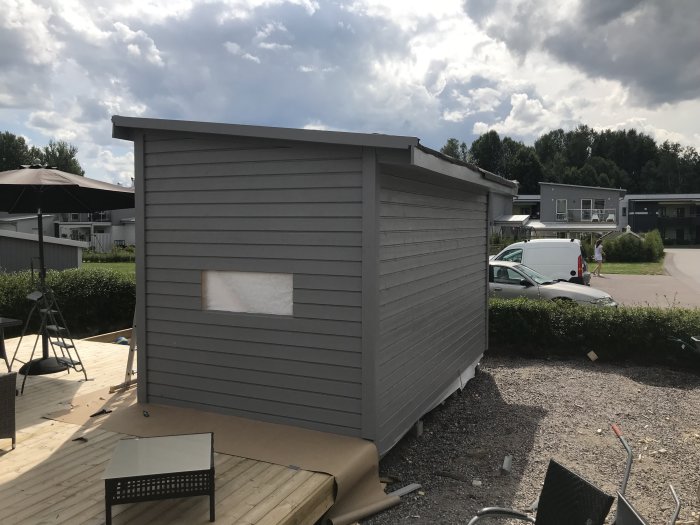 Nybyggt gråmålat friggebod under konstruktion utan fönster och dörr på en solig dag.