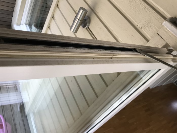 Närbild på en altandörrs övre hörn och fönsterbroms med synliga slitage och skador