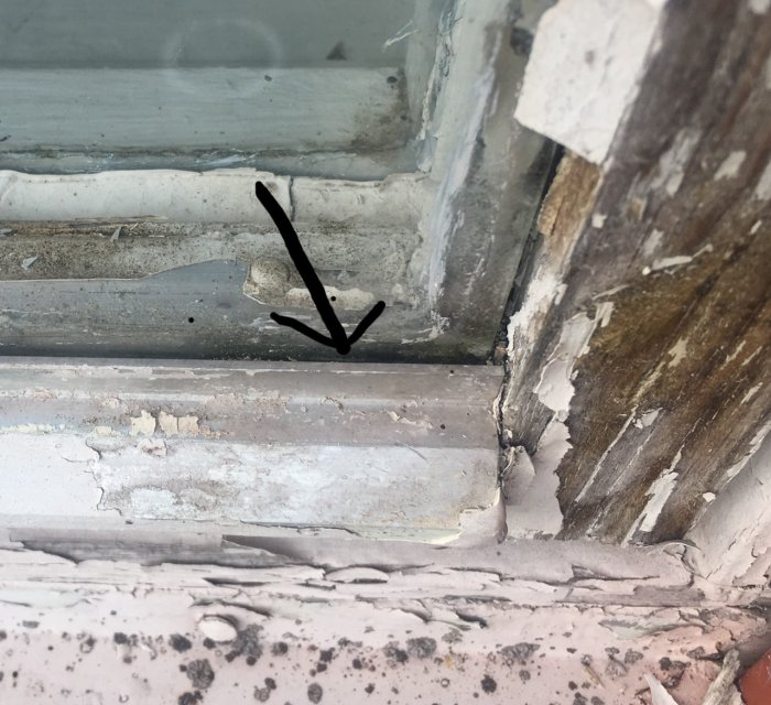 Närbild på nedre delen av ett 60-tals fönster med träram och aluprofil, pil visar glipan mellan metall och glas.