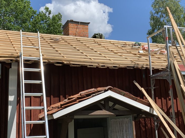 Ny läktad takkonstruktion på röd träbyggnad med arbetsmaterial synligt.