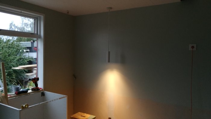 Nybyggt sideboard med verktyg ovanpå och en hängande lampa tänt som lyser upp en vägg.