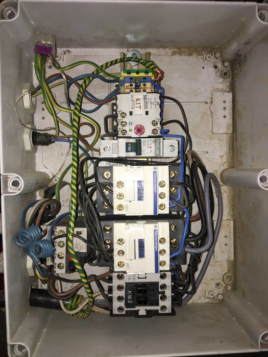 Elcentral med säkringar och trassliga kablar i en grå metallbox.