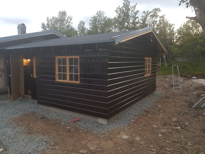 Ett nyrenoverat hus i skymning med mörknande himmel, gruslagd mark runt grunden och en stege till vänster.