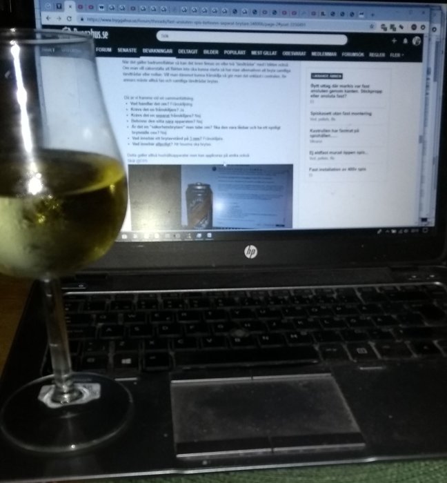 Dator med öppet diskussionsforum på skärmen och ett glas vin i förgrunden.