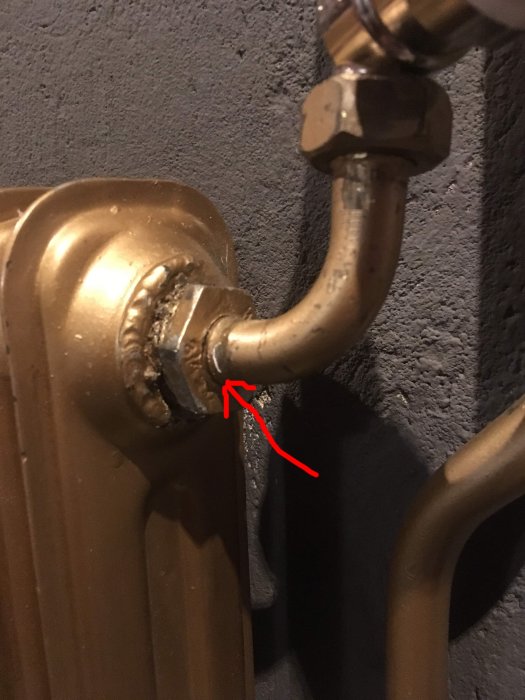 Läckage vid anslutningen mellan radiatorventil och radiator, med synlig tätning och en pil som pekar på läckstället.