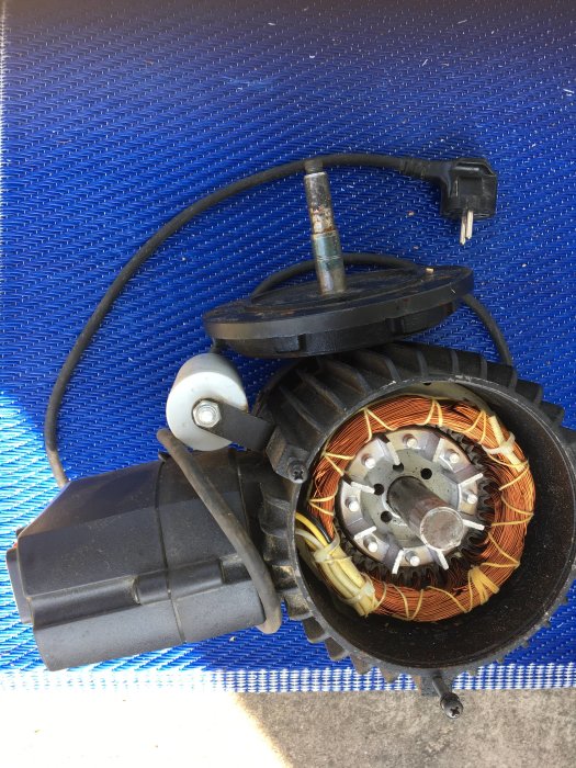 Elektrisk motor demonterad visande koppartrådar och rotorn på blå bakgrund.