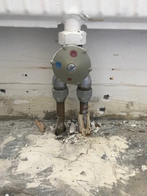 En värmeelementanslutning med en installerad 1-rörsventil mot en vit vägg och stänk av puts.