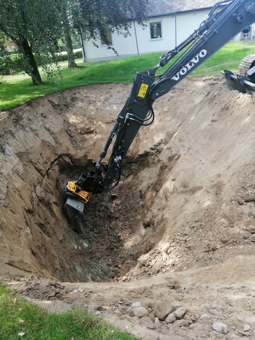 Grävmaskin från Volvo gräver en brunn i skiffermark, nu 6,5 meter djup med synlig berghäll.