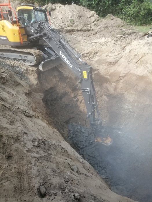 En grävmaskin från Volvo gräver i en stor jordhög med lera och sten.