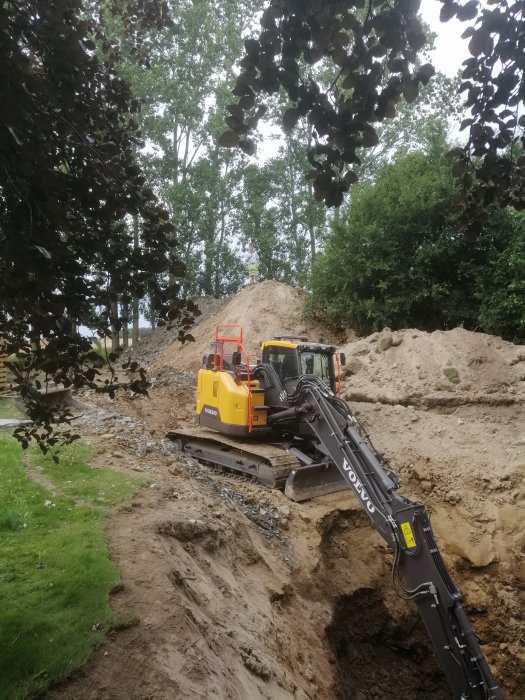 Grävmaskin i arbete vid en grushög och utför grävarbete i skogsmiljö.