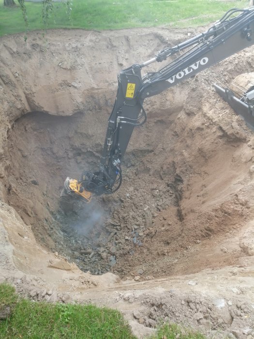 Volvo grävmaskinsarm som arbetar i en stor utgrävning med synlig rök och sprängsten.