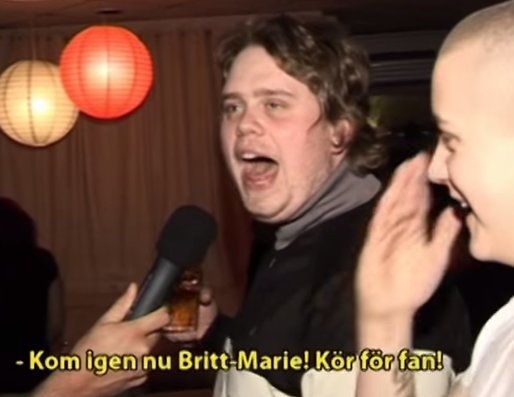 Person med öppen mun och förvånad blick håller en flaska och blir intervjuad, en annan person skrattar.