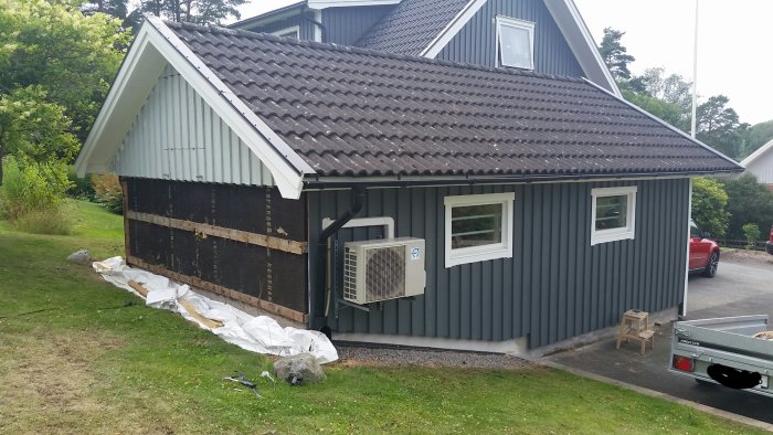 Garage med delvis bytt panel, en vägg klar i grått, den andra avtäckt med isolermaterial synligt och en luftvärmepump.