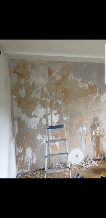 Vägg under renovering med flera lager tapetrester och en stege framför.