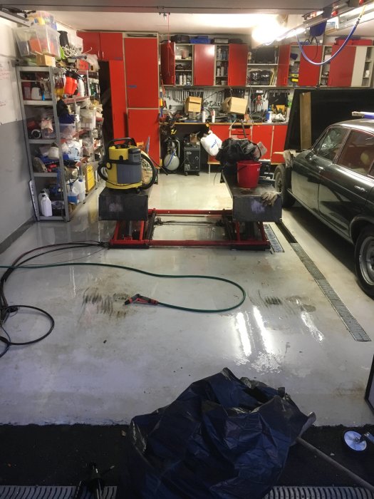 Garage med en klassisk bil, arbetsbänk och verktyg under städning och organisering.