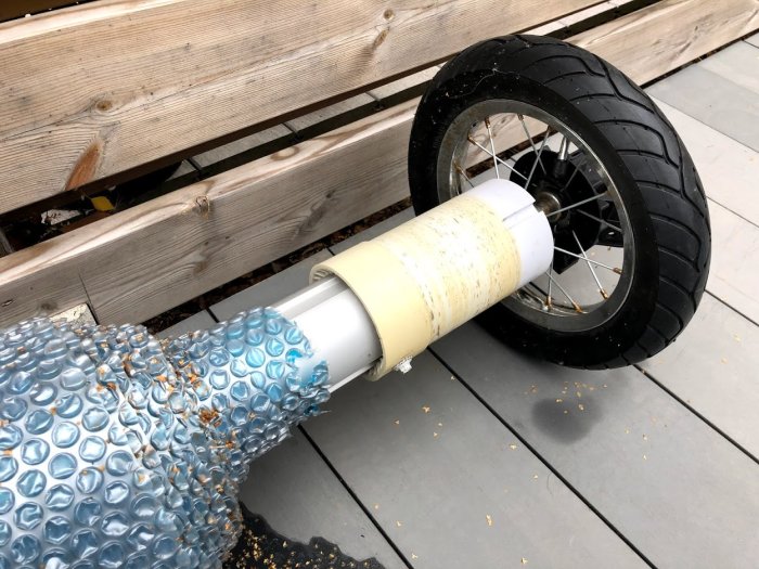 Golfbagshjul fäst vid ett aluminiumrör med ett halvt uppvecklat pooltäcke, mot bakgrund av trätrall.